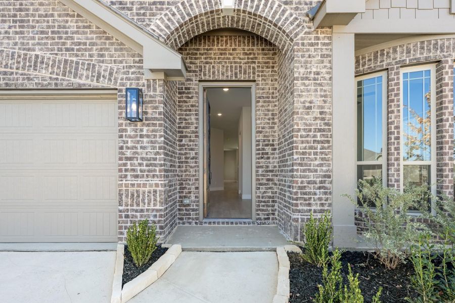 Brick home entrance with arched doorway, wall sconce, and concrete walkway leading to open front door Brick home entrance with arched doorway, wall sconce, and concrete walkway leading to open front door