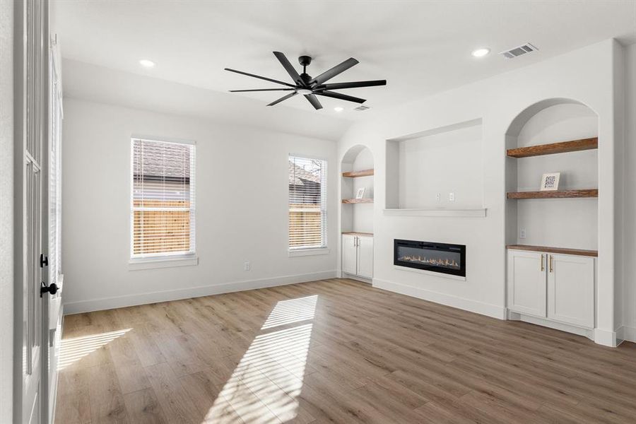 Unfurnished living room featuring ceiling fan, built in features, and light hardwood / wood-style flooring