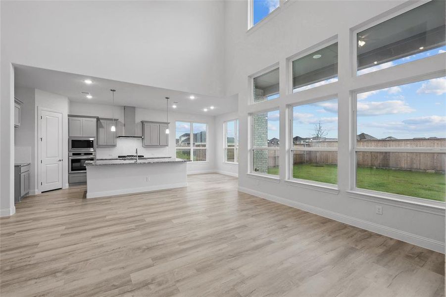 Unfurnished living room with baseboards, light wood-style floors, healthy amount of natural light, and a high ceiling
