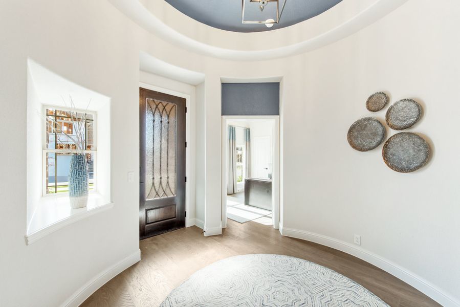 Round foyer with dark wood front door, leaded glass panels, tray ceiling, and hardwood floors