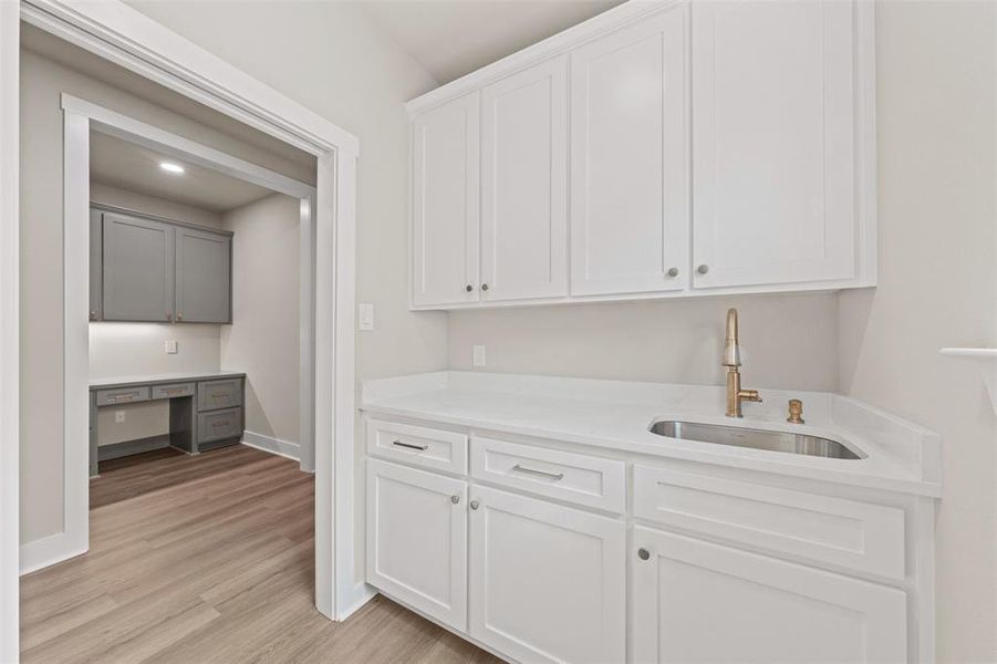 Bar with built in desk, light stone counters, light wood-style floors, and dual tone cabinets