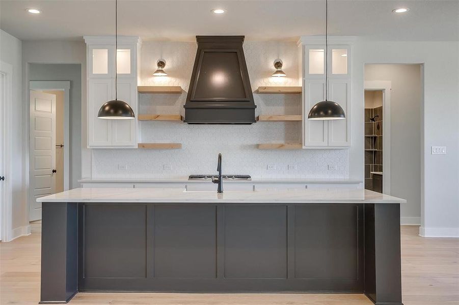 Kitchen featuring backsplash, open shelves, premium range hood, and an island with sink Kitchen featuring backsplash, open shelves, premium range hood, and an island with sink