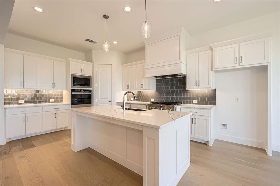 Kitchen with white cabinets, decorative backsplash, light wood-type flooring, and a kitchen island with sink