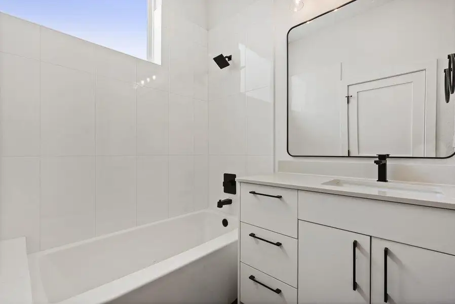 Bathroom featuring a white vanity with black hardware, a rectangular mirror, and a built-in bathtub with a shower
