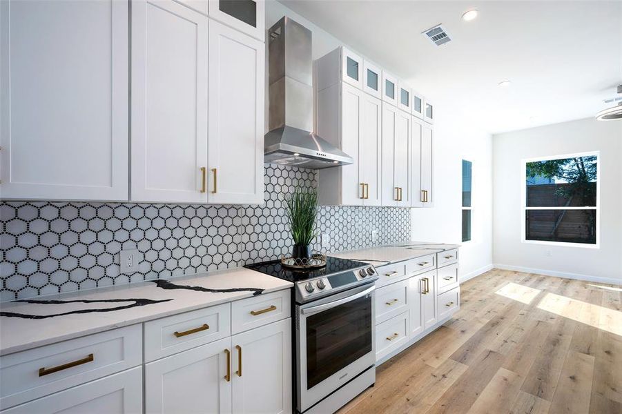 Kitchen featuring light wood-type flooring, white shaker style cabinetry, wall chimney range hood, stainless steel range, and decorative backsplash