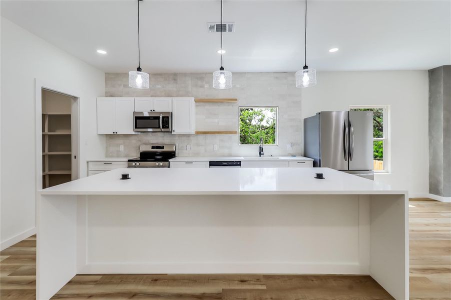 Kitchen featuring white cabinets, stainless steel appliances, backsplash, and light countertops