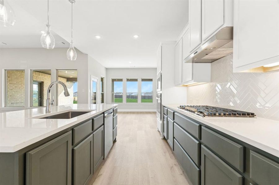 Kitchen with hanging light fixtures, white cabinetry, tasteful backsplash, light wood-style flooring, and light stone countertops Kitchen with hanging light fixtures, white cabinetry, tasteful backsplash, light wood-style flooring, and light stone countertops