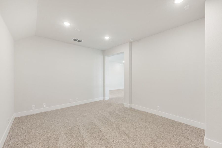 Empty room with white walls, beige carpet, recessed lighting, and an open doorway leading to another room.