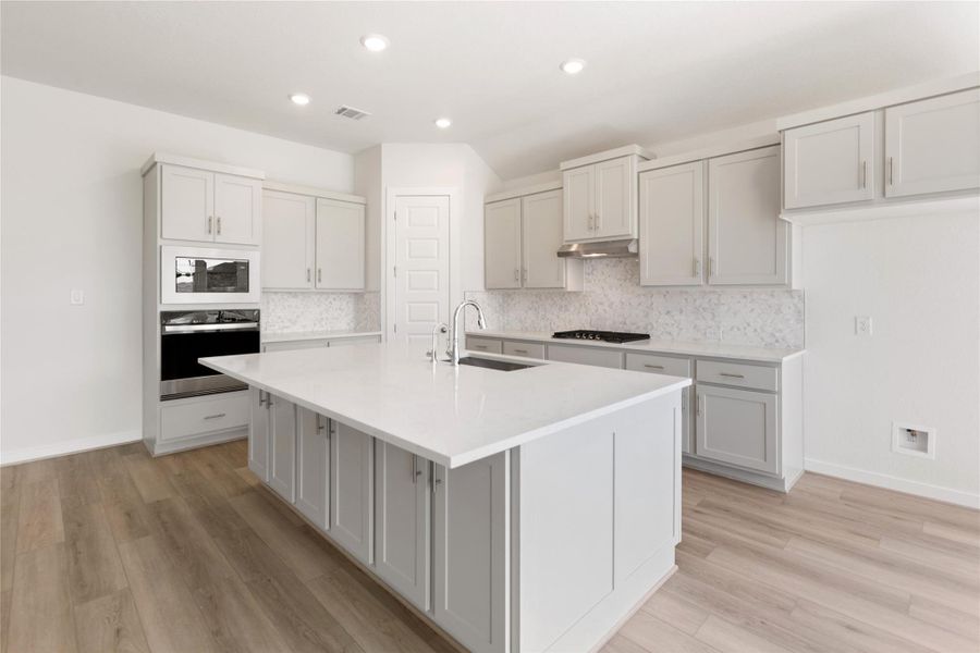 Kitchen with decorative backsplash, stainless steel appliances, recessed lighting, a center island with sink, and light stone countertops