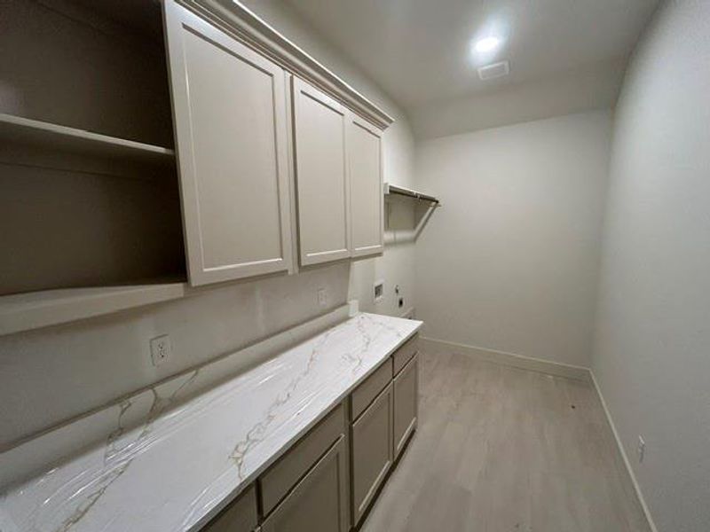 Utility room featuring a stone-look countertop, extensive cabinetry, and wood-finish flooring