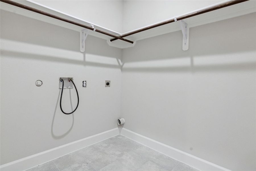 Welcome to a spacious, laundry room with hookups for a washer and dryer. It features tile flooring, and built-in shelving for storage.