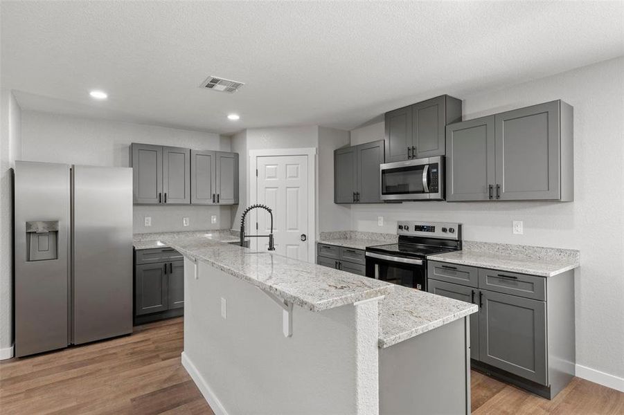 Kitchen featuring stainless steel appliances, gray cabinetry, a kitchen island with sink, light wood-style floors, and light stone countertops Kitchen featuring stainless steel appliances, gray cabinetry, a kitchen island with sink, light wood-style floors, and light stone countertops