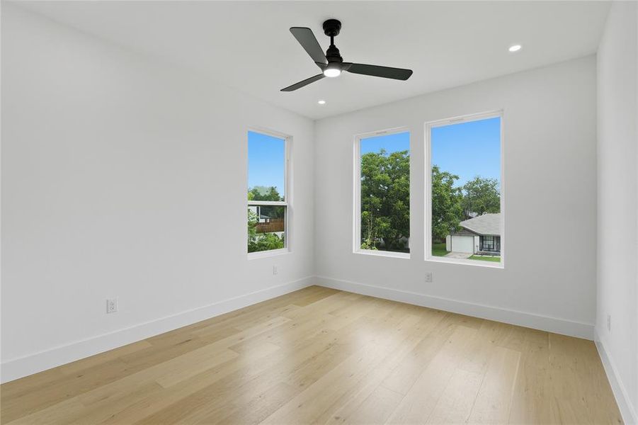 Bright room featuring light wood-finish flooring, white walls, and a modern black ceiling fan Bright room featuring light wood-finish flooring, white walls, and a modern black ceiling fan