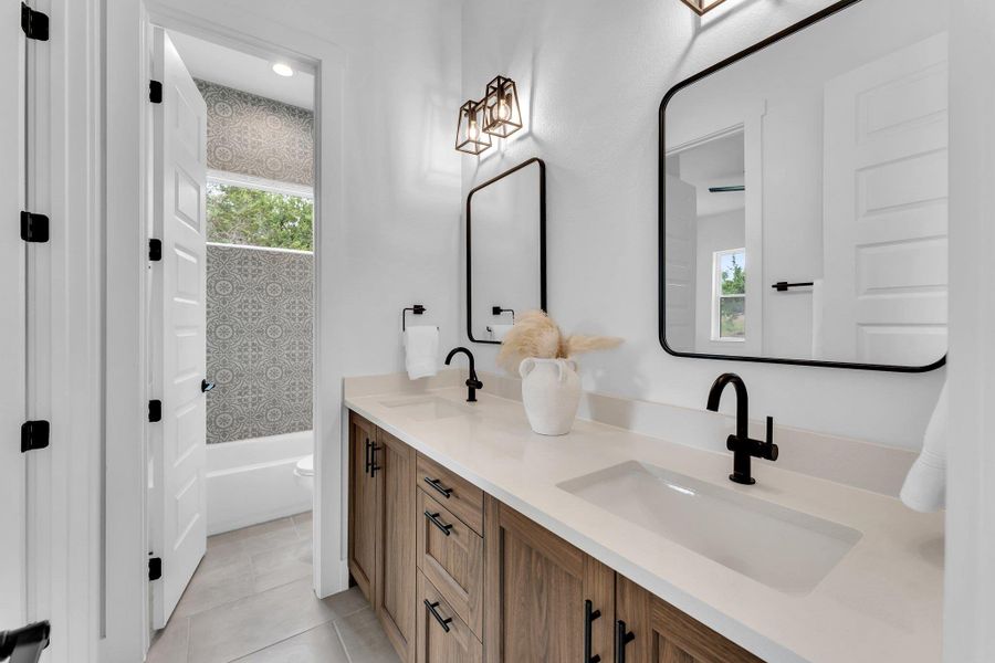 A double vanity with sleek black fixtures and a windowed shower beyond offers practical elegance. A double vanity with sleek black fixtures and a windowed shower beyond offers practical elegance.