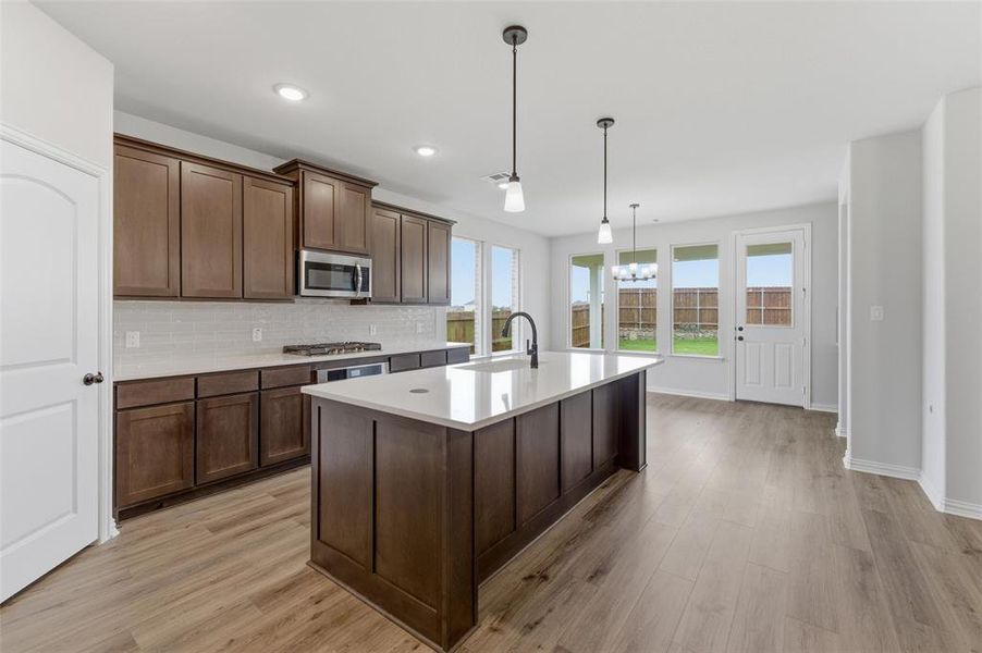 Modern kitchen featuring wood-finish flooring, a large center island with a solid surface countertop, dark wood cabinetry, and a subway tile backsplash