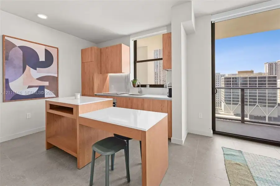 Kitchen featuring wood-finish cabinetry, white countertops, a built-in island with integrated seating, recessed lighting, and a sliding glass door leading to a balcony
