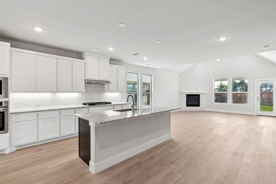 Kitchen featuring white cabinetry, tasteful backsplash, light stone counters, light wood-style floors, and plenty of natural light Kitchen featuring white cabinetry, tasteful backsplash, light stone counters, light wood-style floors, and plenty of natural light