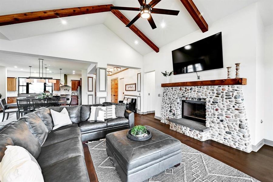 Living area with dark wood-style floors, high vaulted ceiling, recessed lighting, a stone fireplace, and beam ceiling