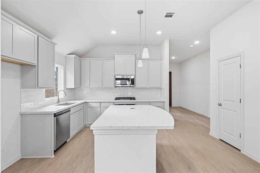 Kitchen featuring a center island, light stone counters, light wood-type flooring, tasteful backsplash, and vaulted ceiling