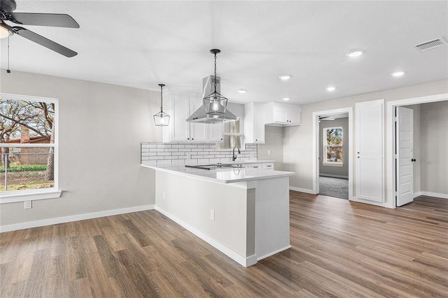 Kitchen featuring white cabinets, a peninsula, backsplash, recessed lighting, and island range hood