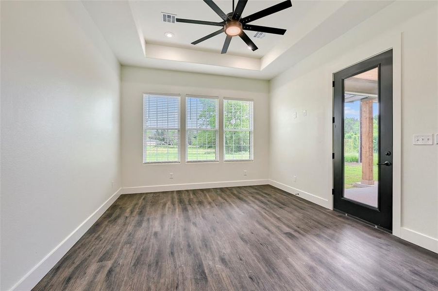 Unfurnished room featuring visible vents, a raised ceiling, dark wood-style flooring, and plenty of natural light