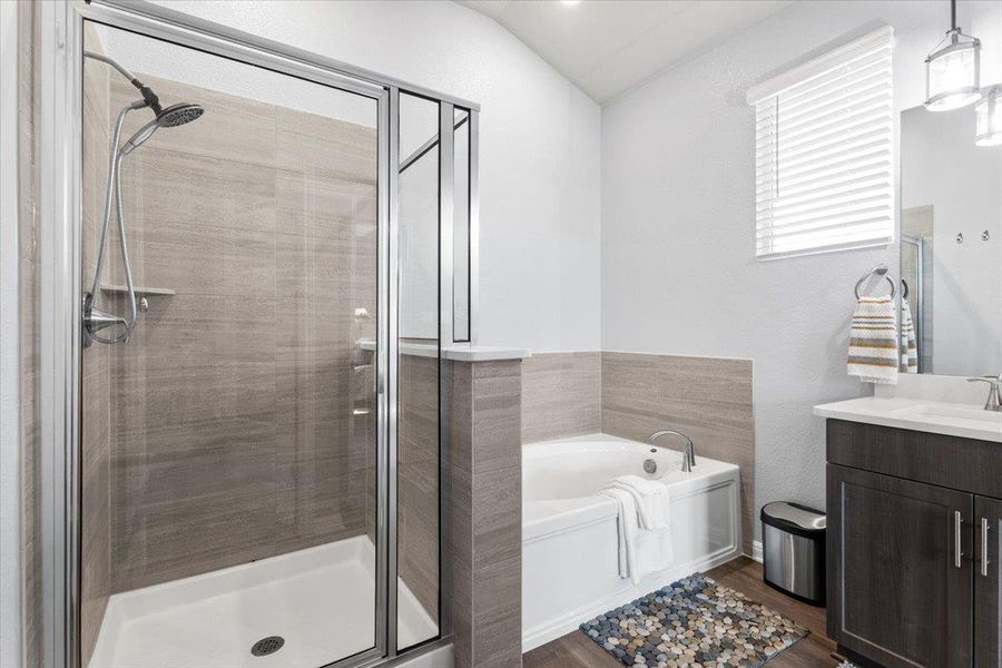 Bathroom featuring a stall shower, lofted ceiling, wood finished floors, a garden tub, and vanity