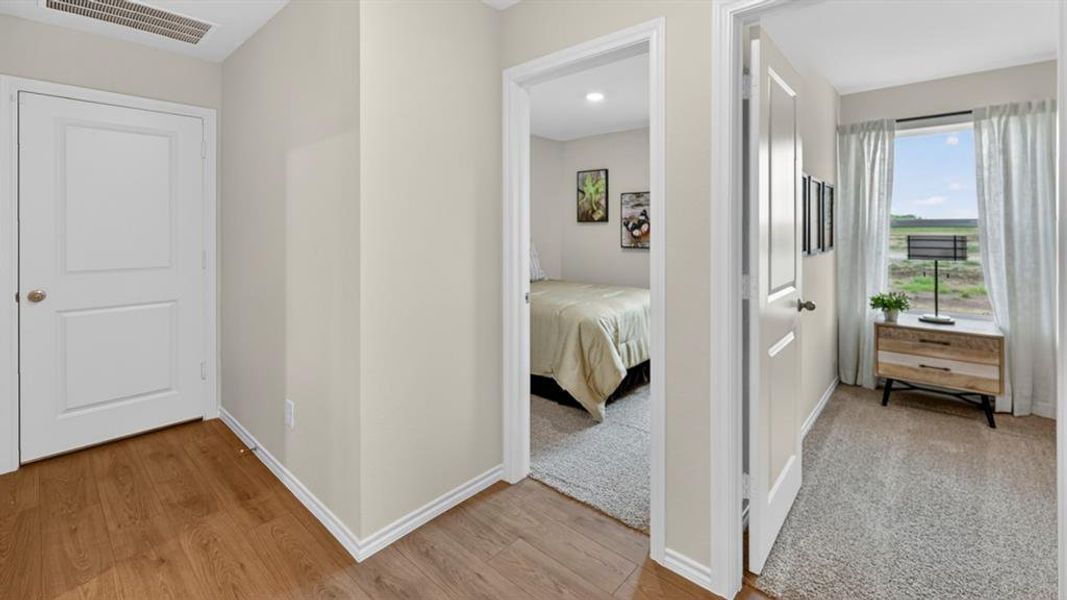 Hallway with wood-finish flooring leading to two rooms with carpeted flooring