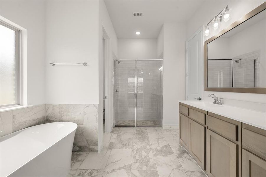 Bathroom with vanity, a freestanding tub, a stall shower, marble look tiles, and recessed lighting