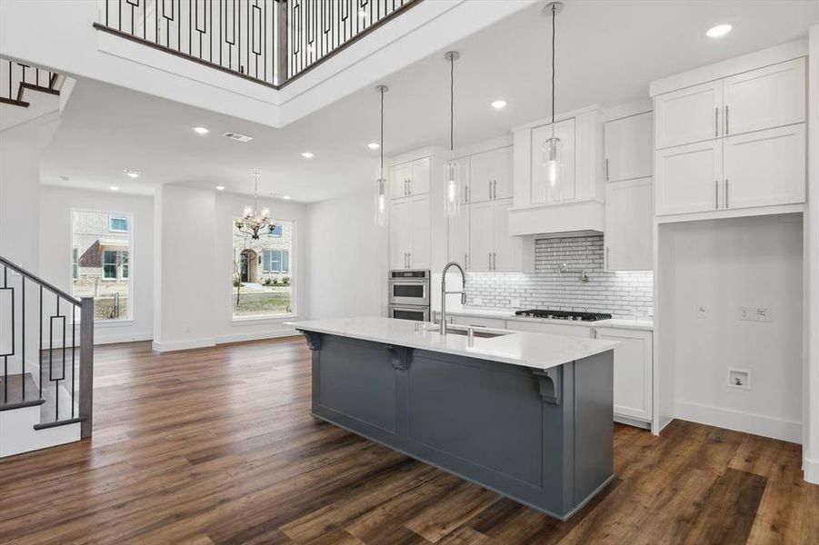 Kitchen featuring a sink, white cabinets, hanging light fixtures, tasteful backsplash, and an island with sink