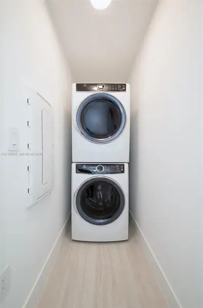 Dedicated laundry alcove featuring a stacked white front-loading washer and dryer set on light-toned wood-finish flooring