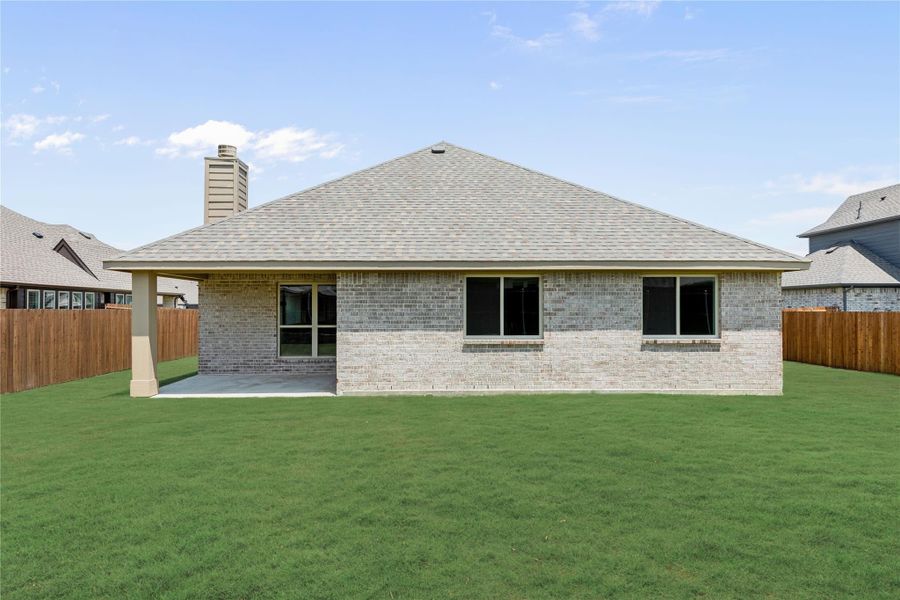 Back of single-story brick home with covered patio, chimney, and fenced backyard with green lawn Back of single-story brick home with covered patio, chimney, and fenced backyard with green lawn