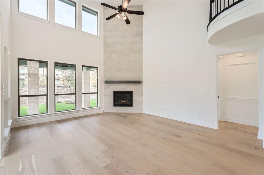 Unfurnished living room featuring a high ceiling, light wood-type flooring, a tiled fireplace, and plenty of natural light