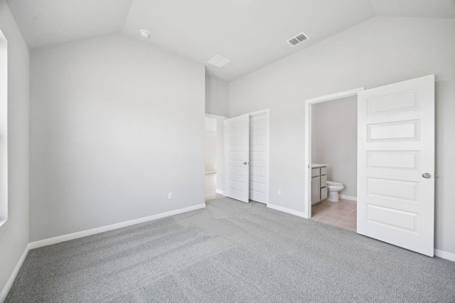 Unfurnished bedroom with vaulted ceiling, light colored carpet, and ensuite bathroom