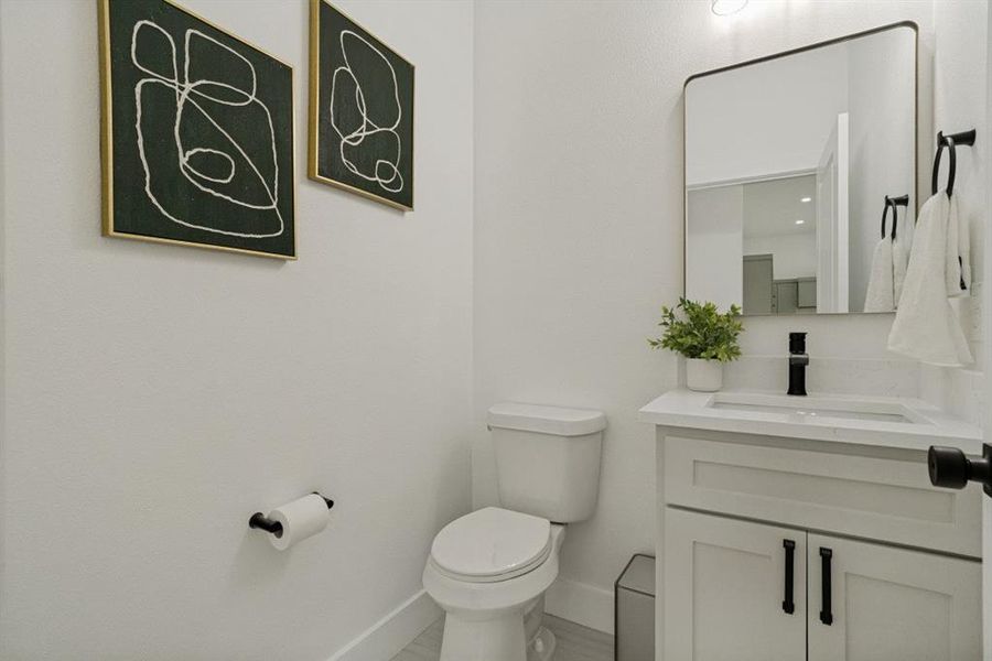 Powder room with a white vanity featuring a light-toned countertop, integrated sink, and matte black faucet Powder room with a white vanity featuring a light-toned countertop, integrated sink, and matte black faucet