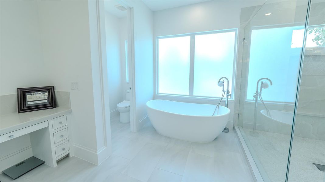 This bright and modern bathroom features a freestanding tub by a large frosted window, a spacious glass-enclosed shower, and a convenient vanity with storage.
