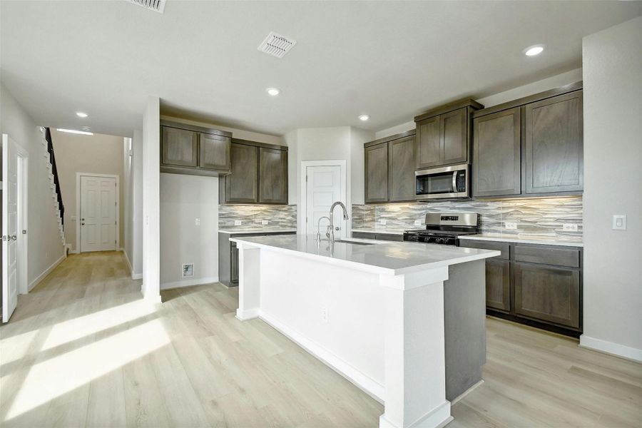 Kitchen featuring decorative backsplash, sink, light hardwood / wood-style flooring, an island with sink, and stainless steel appliances