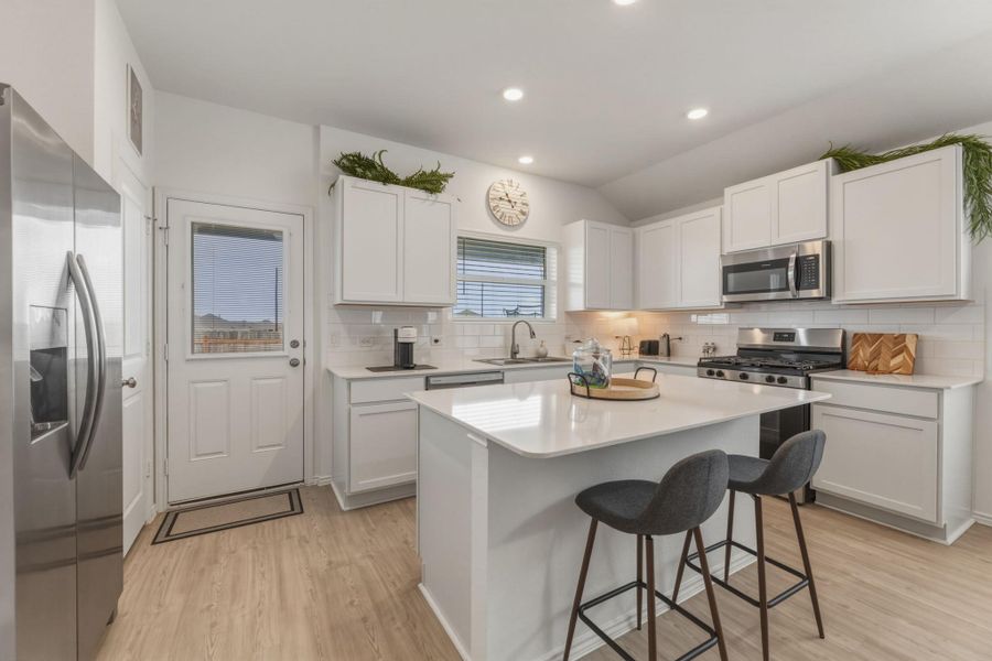 The kitchen features white cabinetry, stainless steel appliances, a center island with countertop seating, and light-toned flooring