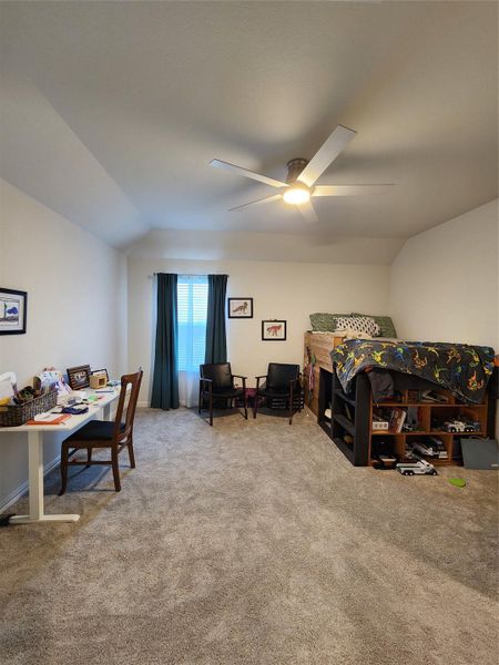 A comfortable bedroom with vaulted ceilings, plush carpeting, and a modern ceiling fan for optimal airflow.