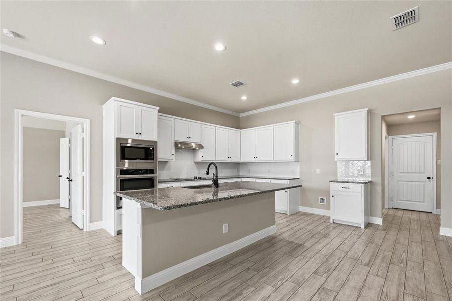 Kitchen with white cabinets, dark stone countertops, stainless steel appliances, backsplash, and crown molding Kitchen with white cabinets, dark stone countertops, stainless steel appliances, backsplash, and crown molding