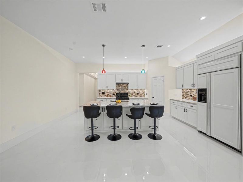 Kitchen with paneled built in fridge, a kitchen bar, pendant lighting, an island with sink, and backsplash
