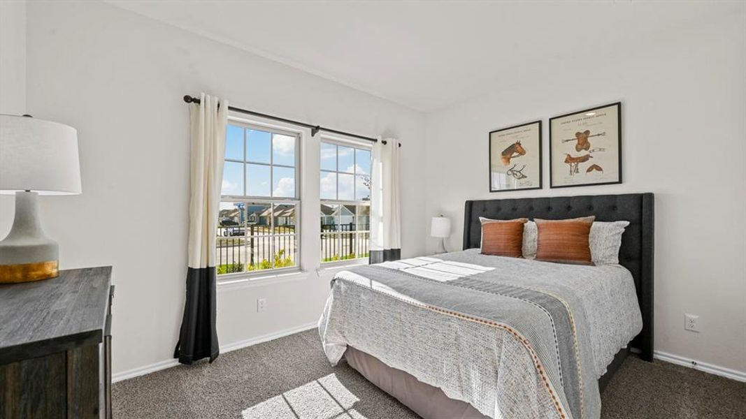 This room features two windows providing ample natural light, a textured headboard, and soft gray carpeting This room features two windows providing ample natural light, a textured headboard, and soft gray carpeting