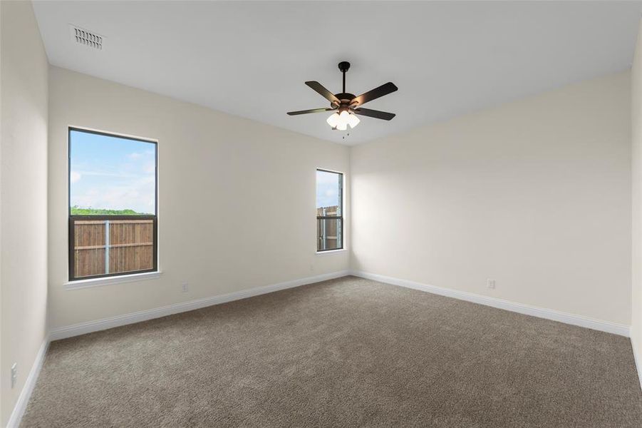 Neutral-toned interior room featuring two large windows, a ceiling fan with integrated lighting, and plush carpet flooring