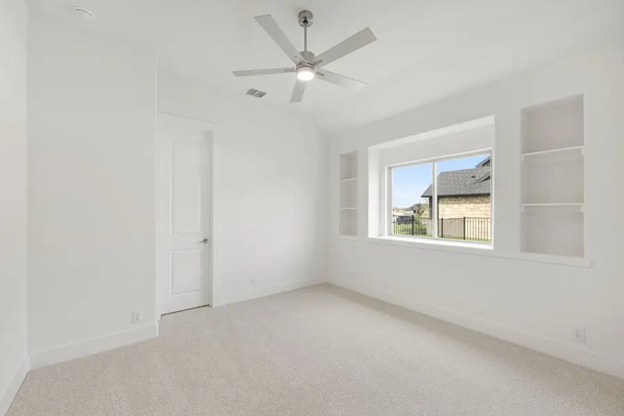 Empty bedroom with vaulted ceiling, ceiling fan, built-in shelves, and carpet flooring Empty bedroom with vaulted ceiling, ceiling fan, built-in shelves, and carpet flooring