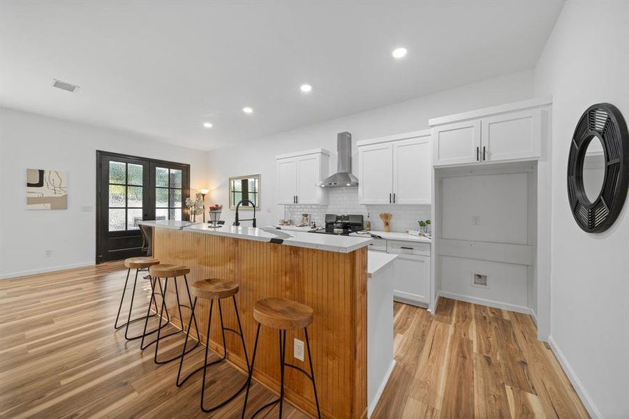 Kitchen with tasteful backsplash, black range with electric cooktop, light hardwood / wood-style flooring, sink, and wall chimney exhaust hood