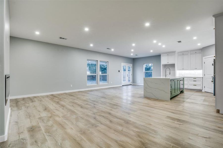 Kitchen featuring white cabinetry, sink, light stone countertops, an island with sink, and light wood-type flooring