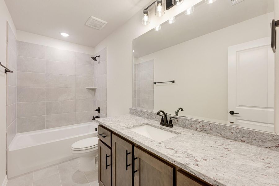 Bathroom with granite countertop vanity, tiled tub-shower combo, and large mirror with pendant lights Bathroom with granite countertop vanity, tiled tub-shower combo, and large mirror with pendant lights