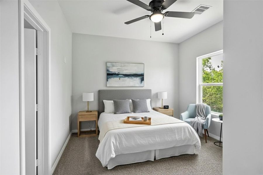 This bedroom is bright and cozy, featuring a large window, neutral walls, and a ceiling fan. **Photo has been staged.**