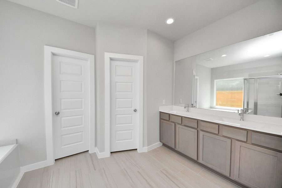 Elevate your daily routine at the elegant vanity, now equipped with double sinks, light countertops, modern hardware, and beautiful recessed lights. Sample photo of completed home with similar floor plan. Actual colors and selections may vary.