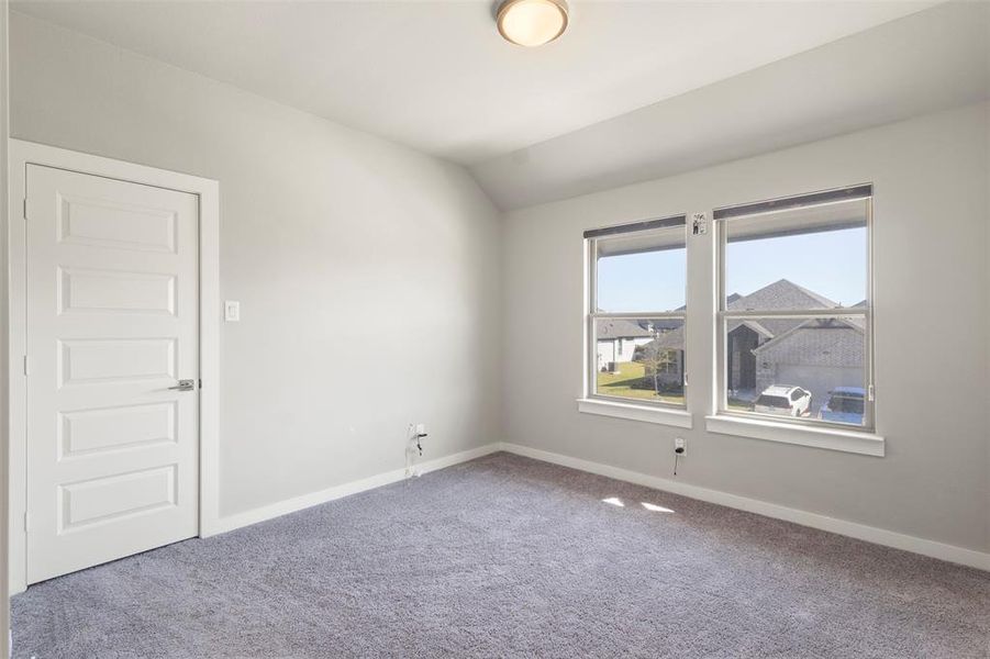 Carpeted empty room featuring vaulted ceiling and baseboards