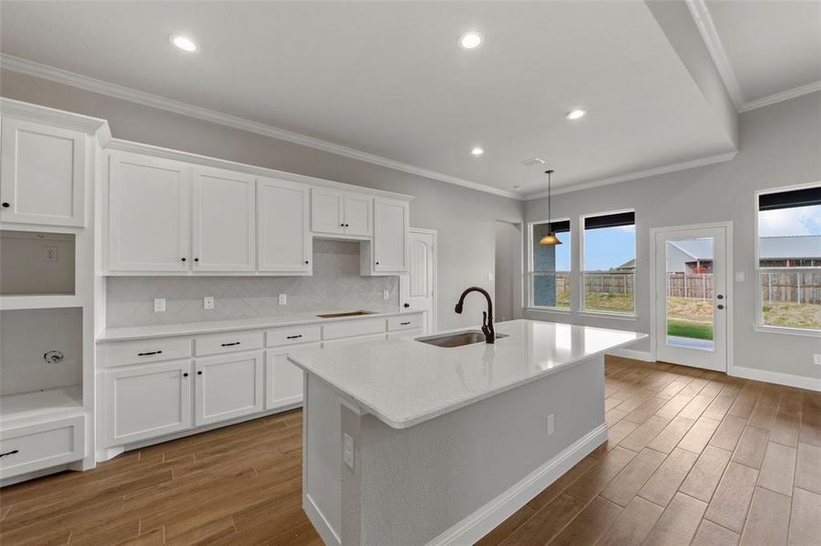 Kitchen with crown molding, sink, white cabinets, and a kitchen island with sink